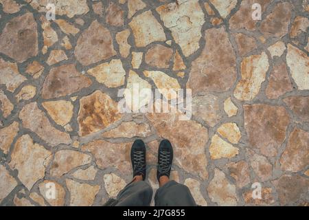 Scatto in alto di piedi maschi con sneakers nere in piedi su pavimento in pietra, spazio copia incluso Foto Stock