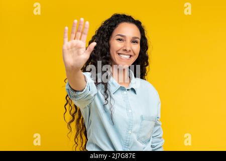Ritratto di felice giovane donna che mostra palma allo studio giallo Foto Stock