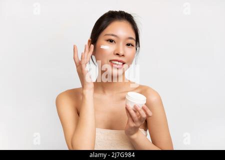 Ritratto di signora asiatica che applica la crema sulla guancia che tiene vaso Foto Stock