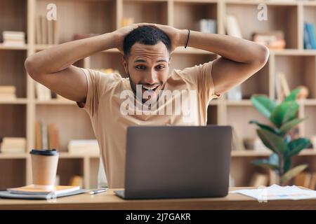 OMG sì, l'ho fatto. L'uomo arabo pieno di gioia che usa il laptop e tocca la testa nell'eccitazione, celebrando le grandi notizie Foto Stock