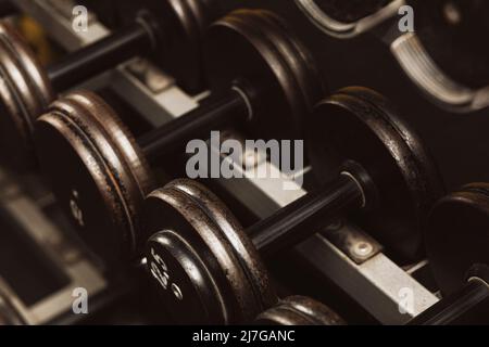 File di manubri di ferro nero su una rastrelliera in palestra, nero con numeri di peso bianchi Foto Stock