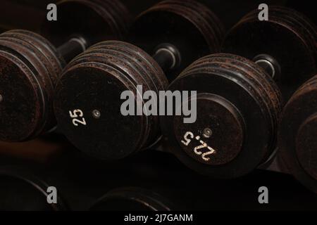 File di manubri di ferro nero su una rastrelliera in palestra, nero con numeri di peso bianchi, primo piano Foto Stock