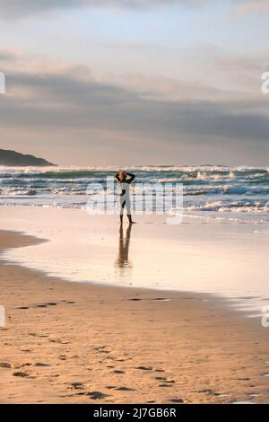 Un uomo che indossa un costume da bagno in piedi sulla riva e guarda verso il mare a Crantock Beach a Newquay in Cornovaglia. Foto Stock