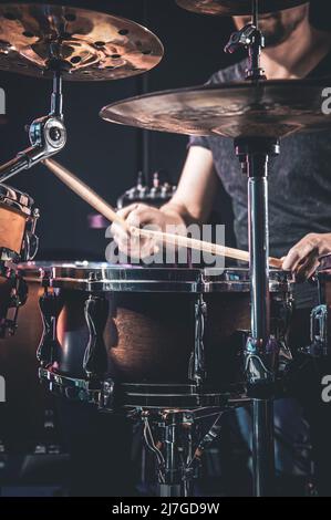 Un batterista maschile suona i tamburi in una stanza buia. Foto Stock