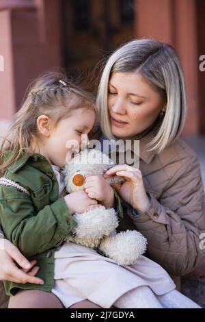 ragazza eccitata che tiene orsacchiotto vicino alla madre all'aperto Foto Stock