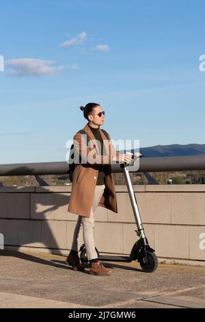 Vista verticale del giovane uomo bello con un'acconciatura a piedi con il suo scooter elettrico AS e trasporto ecologico alternativo Foto Stock