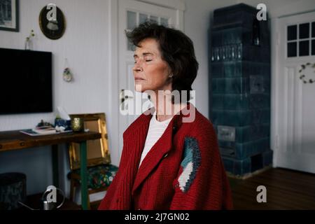 Donna anziana con occhi chiusi meditando a casa Foto Stock