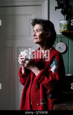 Sorridente anziana che contempla mentre si alza in cucina a casa Foto Stock