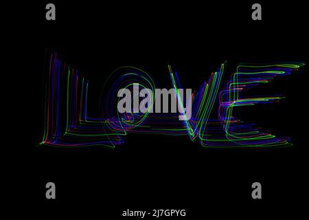 La parola 'Amore' scritta in aria con percorsi di movimento colorati al neon su sfondo nero Foto Stock
