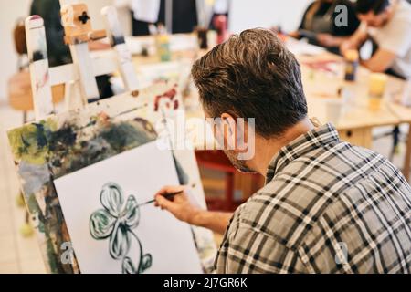 Studente maschio maturo che pratica la pittura sulla tela dell'artista in classe d'arte Foto Stock