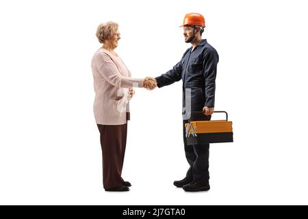 Colpo di lavoratore a profilo completo in un casco uniforme e le mani scuotono con una donna anziana isolata su sfondo bianco Foto Stock