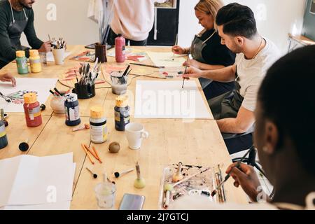 Studenti di sesso maschile e femminile che praticano la pittura mentre si siedono a tavola in classe d'arte Foto Stock