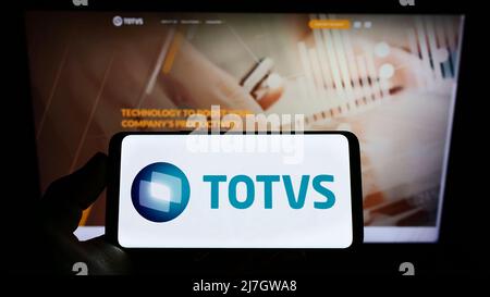 Persona che detiene il cellulare con il logo della società brasiliana di software TOTVS SA sullo schermo di fronte al sito web aziendale. Mettere a fuoco sul display del telefono. Foto Stock