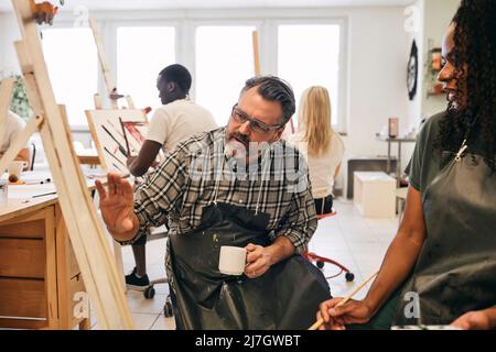 Istruttore maschile che spiega studente femminile sulla tela dell'artista in classe d'arte Foto Stock