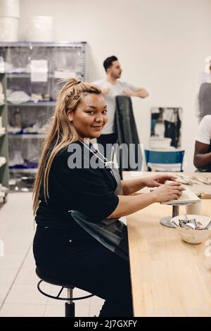 Ritratto di giovane donna sorridente con capelli biondi lunghi che modellano argilla mentre si siede a tavola in classe d'arte Foto Stock