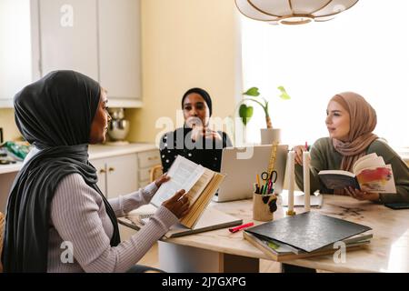 Giovane donna con amici femminili che leggono libri mentre studiano insieme a casa Foto Stock
