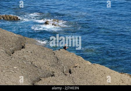 Un pescatore soleggiato con una lunga canna da pesca sulle rocce Magdalena peninsulare Santander Cantabria Spagna in una soleggiata primavera mattina Foto Stock