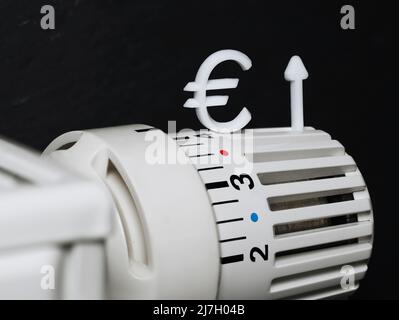 primo piano di un termostato per radiatori con un simbolo dell'euro e una freccia in alto simboleggiano l'aumento dei costi di riscaldamento, concetto di aumento dei prezzi dell'energia in futuro Foto Stock