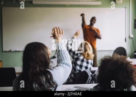 Vista posteriore della ragazza che solleva la mano mentre si siede con gli studenti in aula Foto Stock