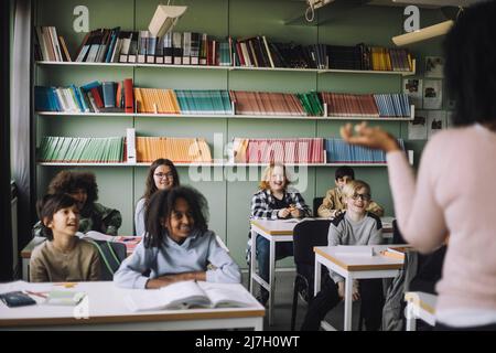 Sorridendo gli studenti che frequentano le lezioni seduti alla scrivania in aula Foto Stock