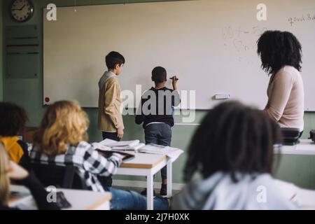 Gli studenti che risolvono la somma matematica in lavagna bianca in classe Foto Stock