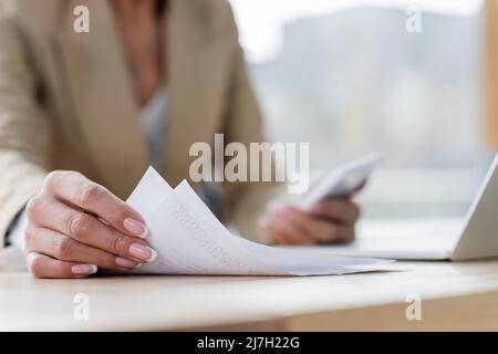 vista ritagliata del banchiere che lavora con documenti e gadget sfocati in ufficio Foto Stock