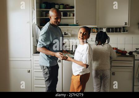 Figlio che aiuta il padre mentre tiene i piatti in cucina a casa Foto Stock