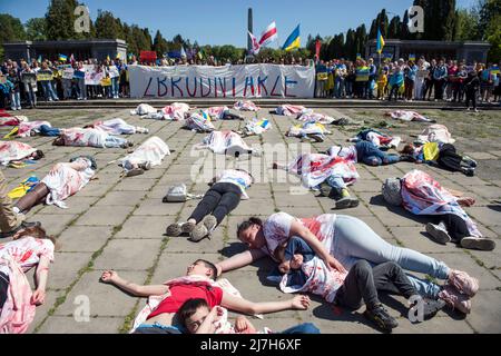 Le persone si trovano sul terreno, in quanto simboleggiano le vittime civili della guerra in Ucraina. Centinaia di ucraini e attivisti polacchi hanno protestato in un cimitero di Varsavia contro i soldati dell'Armata Rossa che sono morti durante la seconda guerra mondiale L'ambasciatore russo in Polonia, Sergey Andreev, è stato colpito con vernice rossa da manifestanti contrari alla guerra in Ucraina in un evento annuale della Giornata della Vittoria che commemorava la fine della seconda guerra mondiale L'ambasciatore Sergey Andreev è arrivato al cimitero dei soldati sovietici per deporre i fiori il giorno della Vittoria, ma il diplomatico e la sua delegazione sono stati costretti a lasciare la zona, accompagnati da ufficiali di polizia. (Foto Foto Stock