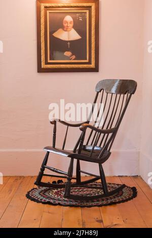 Sedia a dondolo antica su tappeto tondeggiante e ritratto religioso su parete in camera all'interno del vecchio 1790 Maison Rosalie-Cadron House Museum, Lavaltrie, Quebec. Foto Stock