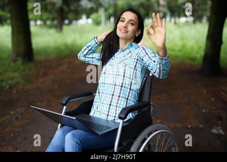 Donna in sedia a rotelle mostra un gesto ok con la mano, il lavoro durante la riabilitazione Foto Stock