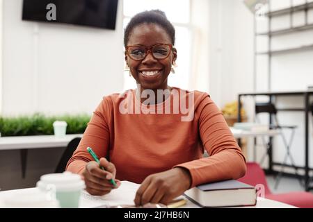 Vista frontale ritratto di giovane donna nera che studia in università e sorride felicemente alla macchina fotografica Foto Stock