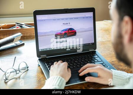 Grecia, Atene, gennaio 23 2022. SCELTA DI VEICOLI TESLA. Ad, auto elettrica rossa Tesla modello 3 online. PC sul tavolo, mano sulla tastiera Foto Stock