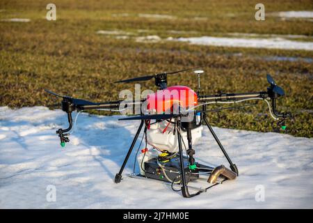 Sul campo si erge un bell'agrodro rosso. Il grano cresce. La neve non si è ancora sciolta. Agrodron è pronto a spruzzare fertilizzante. Foto Stock