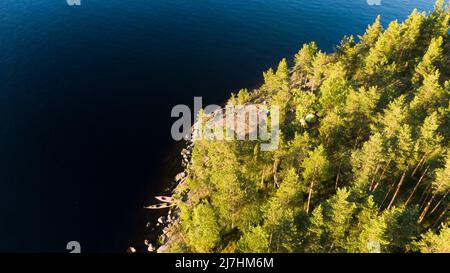 Campeggio con tende su un'isola rocciosa in estate in una foresta di conifere, kayak vicino alla riva vista aerea, week-end all'aperto Foto Stock