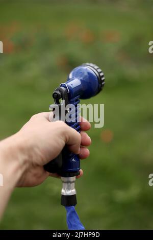 La mano del giardiniere tiene un tubo con un'irroratrice ed innaffiato le piante nel giardino Foto Stock