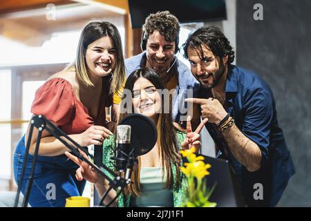 Un team di quattro presentatori saluta il pubblico del loro podcast vlog live streaming via internet - un gruppo di influencer parla nel microfono Foto Stock