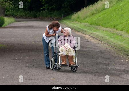 donna fuori con signora molto anziana in sedia a rotelle Foto Stock