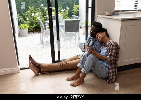 Giovane donna afroamericana che riposa testa sulla spalla del ragazzo mentre si fa un caffè a casa Foto Stock