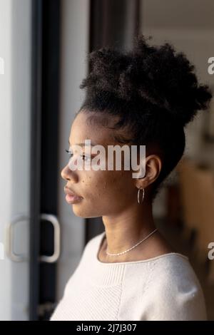 Primo piano di una giovane afroamericana seria e premurosa che guarda attraverso la finestra a casa Foto Stock