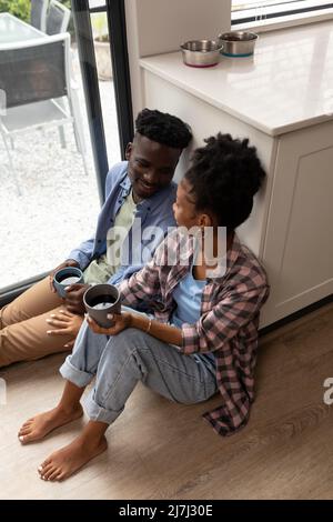 Vista ad alto angolo della giovane coppia afroamericana sorridente con caffè che si guardano a casa Foto Stock