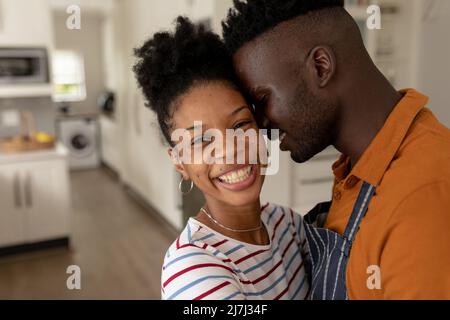 Ritratto di allegra ragazza afroamericana abbracciando giovane ragazzo in cucina a casa Foto Stock