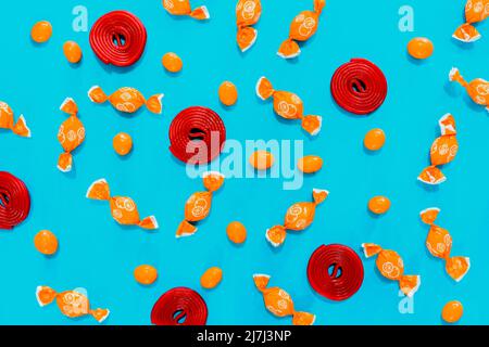 Caramelle, caramelle arancioni e girelli rossi su sfondo blu. Assortimento di caramelle. Carta da parati per usare il testo. Foto Stock