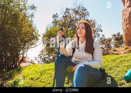 giovane ragazza dai capelli rossi seduta in un prato dopo un'escursione nelle sue vacanze estive. sensazione di libertà e riposo. Foto Stock