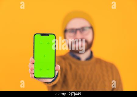 Uomo maturo bearded sfocato e irriconoscibile vestito in abiti casual tenendo uno smartphone con uno schermo verde mockup verso la fotocamera. Foto di alta qualità Foto Stock