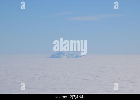 Vista dall'alto della vetta di una montagna innevata che si alza dalle nuvole. Pictire preso da un volo. Foto Stock