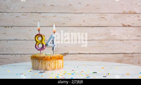 Happy compleanno cifre argento su tavole bianche spazio copia di sfondo. Bella tessera di compleanno con un cupcake con una candela che brucia Foto Stock