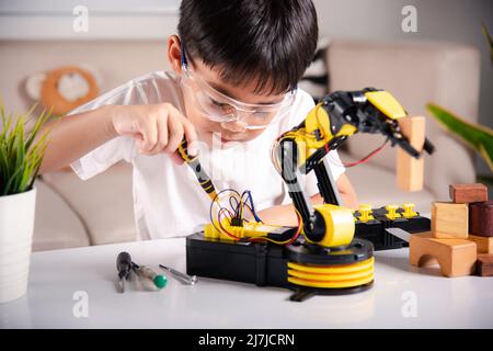 Bambino imparando riparare ottenendo il braccio robot di controllo della lezione, ragazzo piccolo asiatico felice usando il cacciavite per fissare le viti braccio della macchina robotica in casa WO Foto Stock