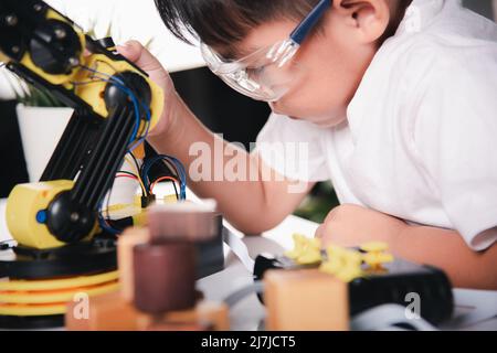 Bambino imparando riparare ottenendo il braccio robot di controllo della lezione, ragazzo piccolo asiatico felice usando il cacciavite per fissare le viti braccio della macchina robotica in casa WO Foto Stock