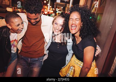 Divertimento venerdì sera. Gruppo di giovani vivaci che ridono con gioia mentre camminano insieme in città di notte. Quattro amici multiculturali che vanno fuori a. Foto Stock