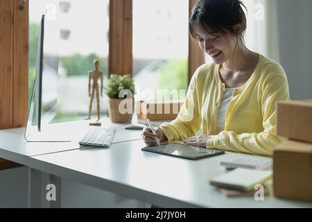 Giovane designer creativo asiatico che tiene la penna stilo disegnando sullo schermo del tablet digitale mentre si siede in un ufficio moderno. Foto Stock